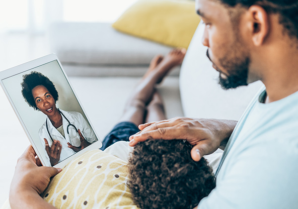 Dad with child talking to a clinician and using telemedicine